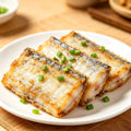 Pan-seared beltfish steaks garnished with spring onion on a white plate